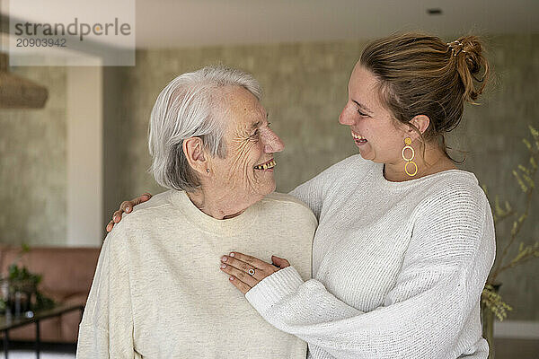 Elderly man and young woman smiling and embracing in a cozy home setting.