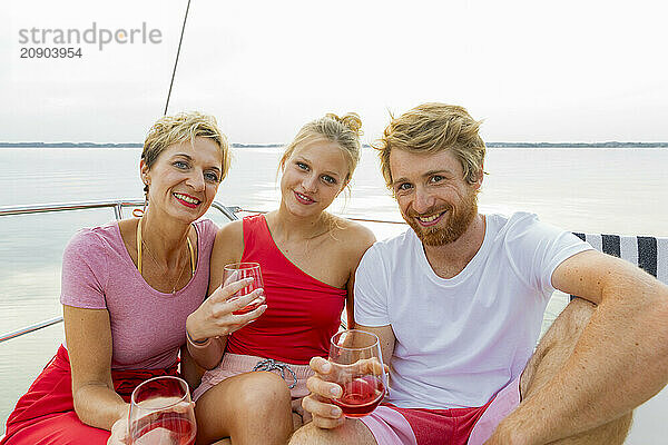 Three friends enjoying drinks on a boat with a lake in the background.