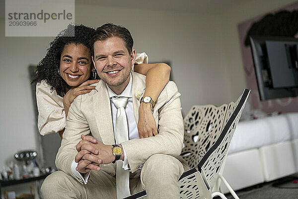 Smiling couple in elegant attire playfully posing in a cozy living room with modern decor.