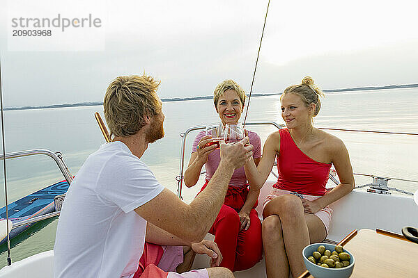 Three friends enjoying a toast with drinks on a sailboat at sunset