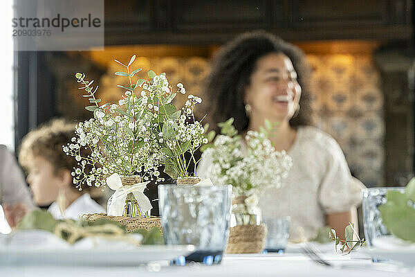 A joyful woman laughing at a festive table adorned with flowers and elegant settings.