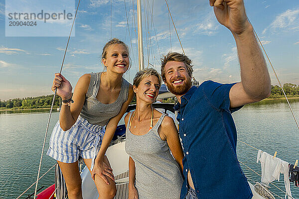 Three happy adults pose for a photo on a sailboat  with a clear blue sky and serene water in the background.