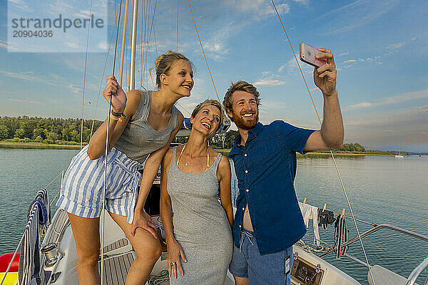 Three friends taking a selfie on a sailboat at sunset  enjoying a serene lake setting.