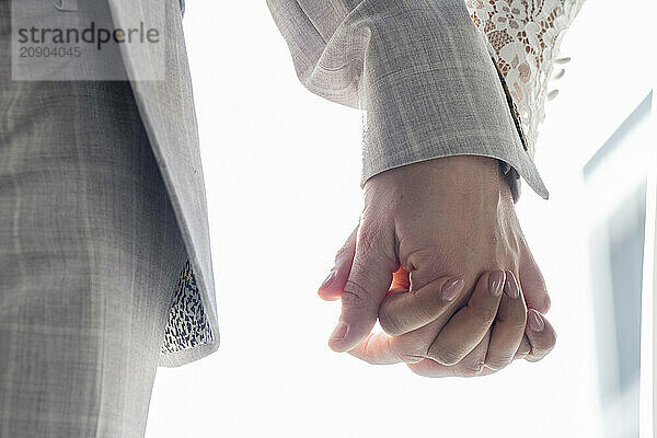 Close-up of a man and woman holding hands  backlit by soft light  suggesting intimacy and connection.