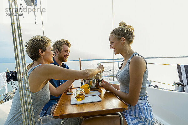 Friends enjoying a meal together on a boat with a view of the water and mountains at sunset.