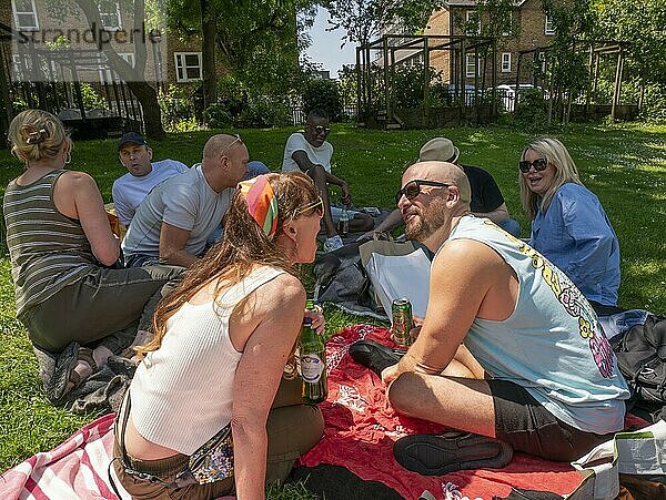 A group of friends enjoying a picnic on a sunny day in a grassy park with buildings in the background.