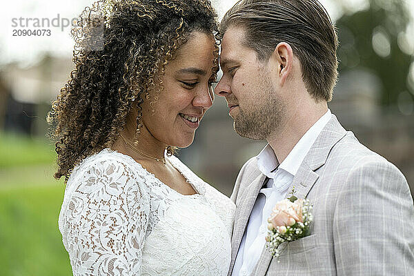 A loving couple embraces on their wedding day  with the woman in a white lace dress and the man in a grey suit.