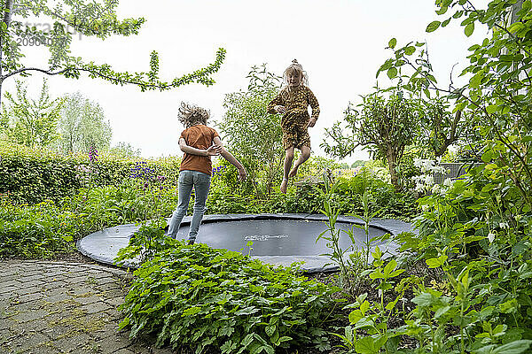 Two children joyfully jumping on an outdoor trampoline surrounded by lush greenery in a backyard garden.