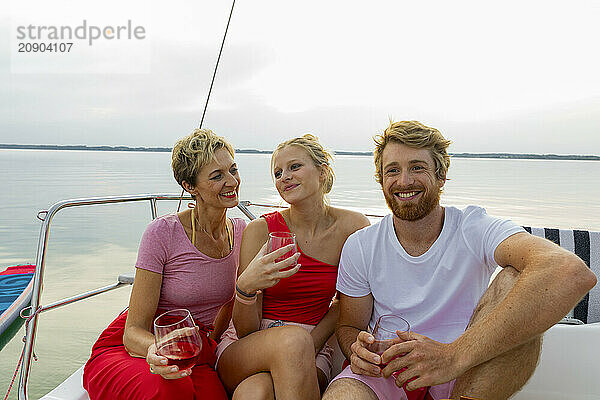 Three friends enjoying drinks while lounging on a sailboat at dusk.