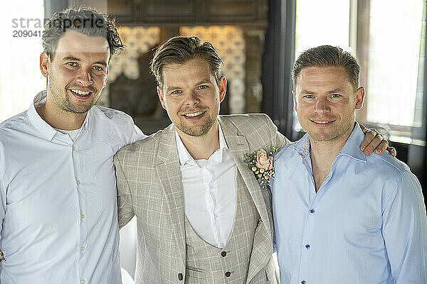 Three smiling men dressed in smart casual attire posing together for a photo.