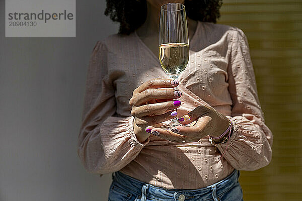 Woman holding a glass of champagne  focusing on her hands with vibrant purple nail polish and sophisticated golden accessories  against a blurred background.