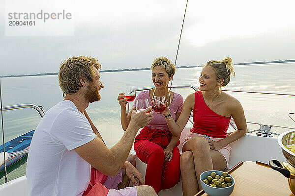 Three friends enjoying drinks and conversation on a boat at sunset.