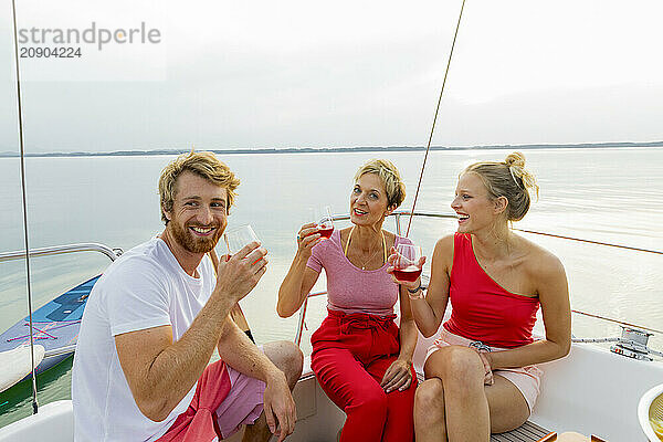 Three friends enjoying drinks on a yacht with a serene lake in the background at sunset.