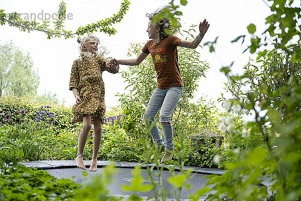 Two people jumping on a trampoline in a lush garden.