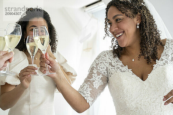 Bride in a white dress and her bridesmaid holding champagne glasses and toasting on a wedding day.