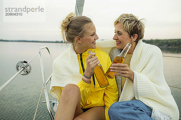 Two women wrapped in a blanket share a moment with a drink on a boat