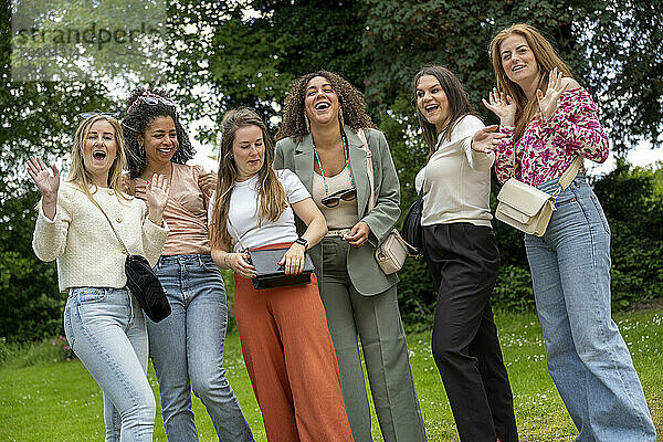 A group of six women laughing and posing together in a park  displaying camaraderie and joy.