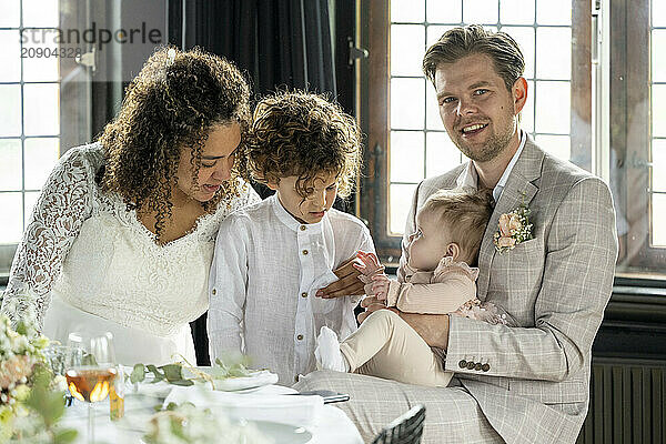 Family dressed in formal attire enjoys a moment together with a baby at a celebratory event.