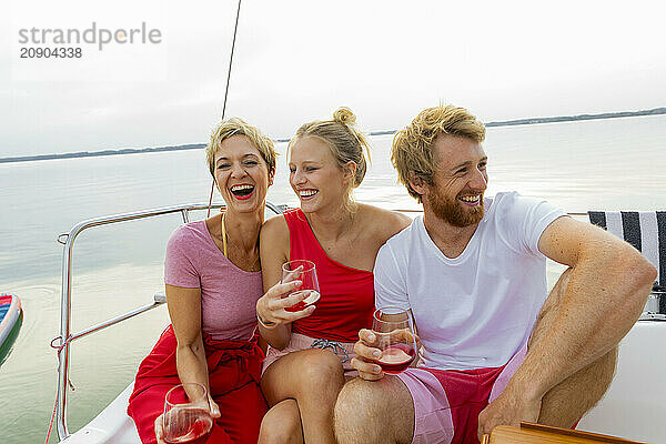 Three friends share a laugh on a sailboat with glasses of wine in hand  enjoying a day on the water.