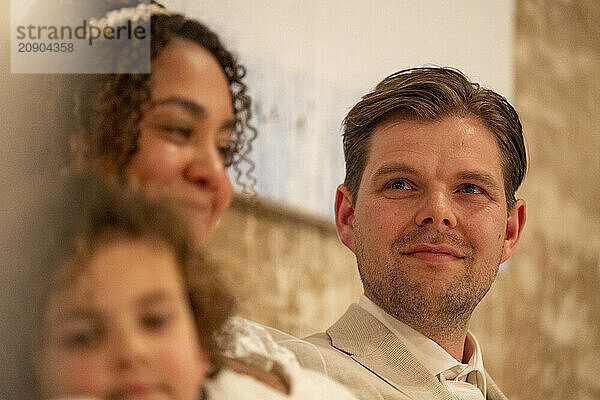 Smiling family enjoying a moment together with partial focus on a man in the foreground  while a woman and child are slightly out of focus beside him.