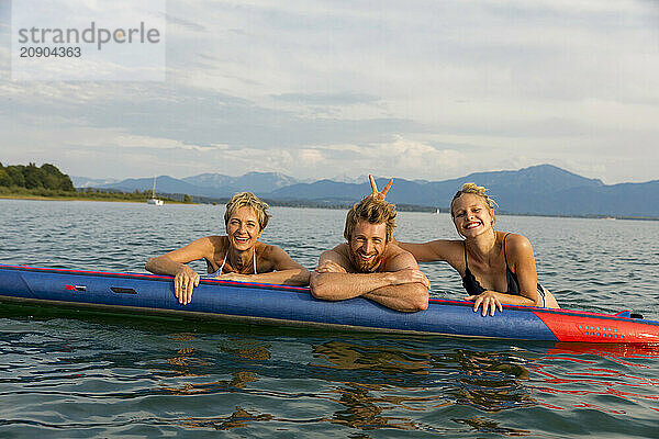 Three friends smiling and posing with a kayak on a sunny day at the lake.