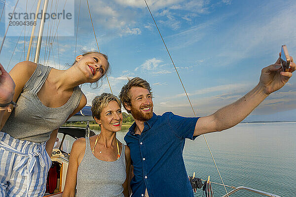 Three friends smiling and taking a selfie on a boat with clear skies in the background.