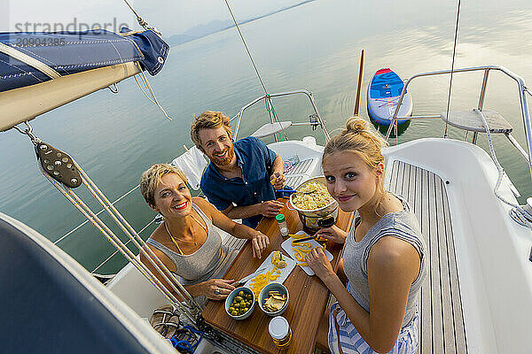 Group of friends enjoying snacks and drinks on the deck of a yacht at sea during a sunny day.