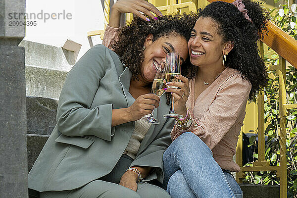 Two women laughing and toasting with champagne glasses on a sunny day outdoors.