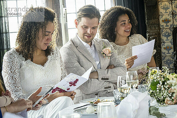 A group of three people enjoying a social event  possibly a wedding  as they share smiles while looking at documents.