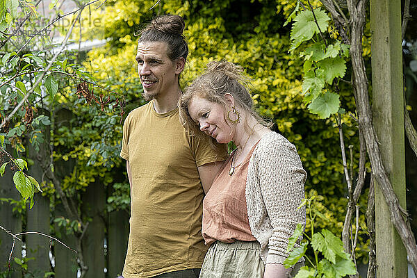 A smiling couple stands close together in a lush garden with a backdrop of green foliage.