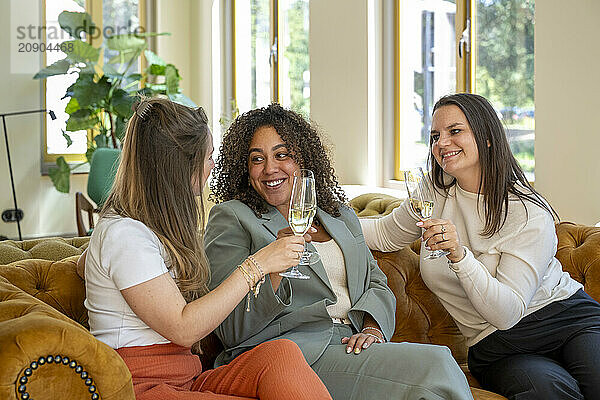 Three women enjoying a conversation and drinking champagne in a bright  stylish living room.