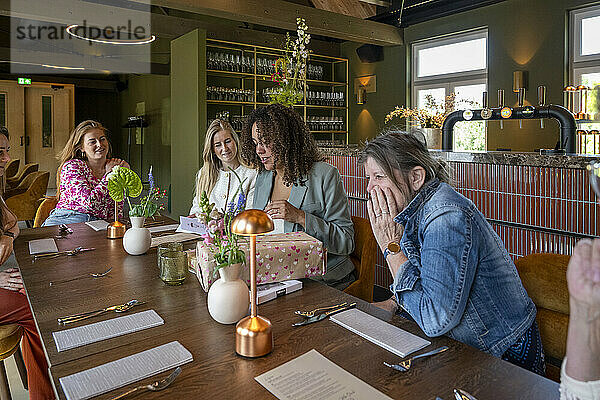 Group of women enjoying a surprise gift at a cozy restaurant table.