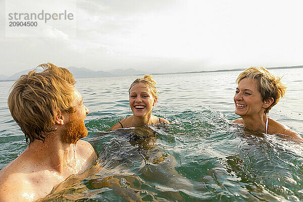 Three people enjoy swimming in the sea  laughing together during a bright sunny day.