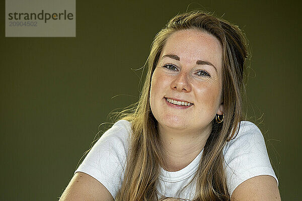 Smiling woman with long hair wearing a white shirt posing against a green background.