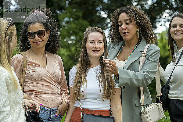 A group of women enjoying a conversation outdoors with trees in the background.