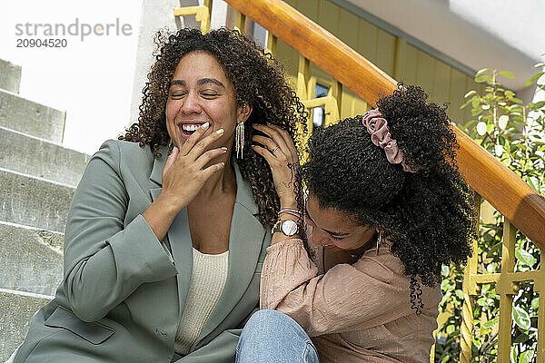 Joyful woman laughing while embracing a young girl on outdoor stairs  both showing happy expressions.