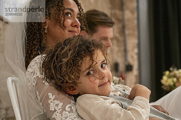 Young child leaning on an adult's lap during a formal event  with another adult in the background.