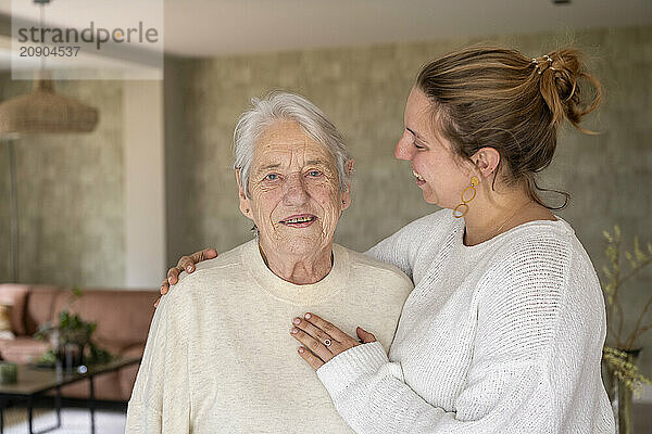 An elderly man and a younger woman smiling together in a cozy living room.