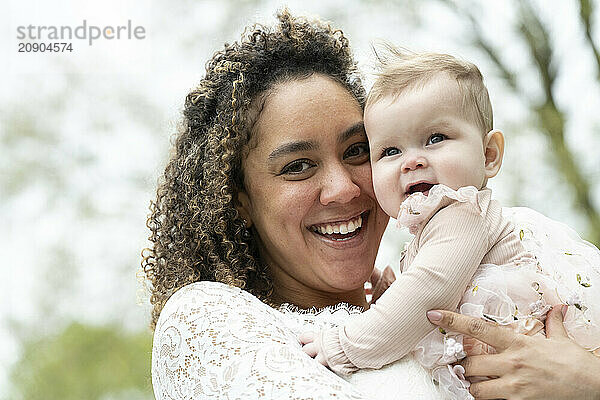 Smiling woman holding a happy baby outdoors on a blurred natural background.