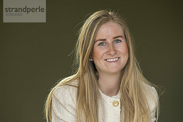 Smiling woman with long blonde hair wearing a white sweater against a green background.