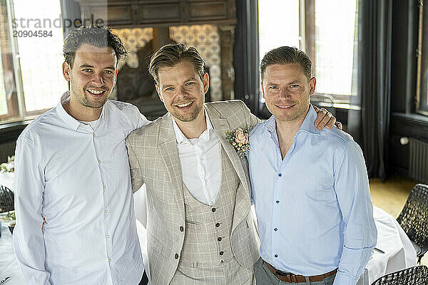 Three smiling men dressed in formal attire posing together indoors  possibly at a celebratory event.