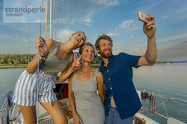 Three friends taking a selfie on a sailboat at sunset  smiling and gesturing peace signs.