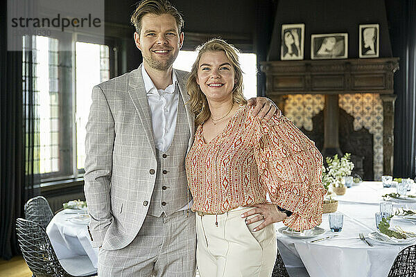 Smiling couple standing together in an elegant dining room with a table set in the background.