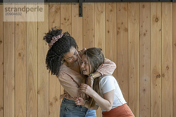 Two women sharing a joyful hug in a room with wooden walls.