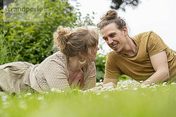 A smiling man and woman lie on the grass  looking at each other and enjoying a pleasant conversation outdoors.