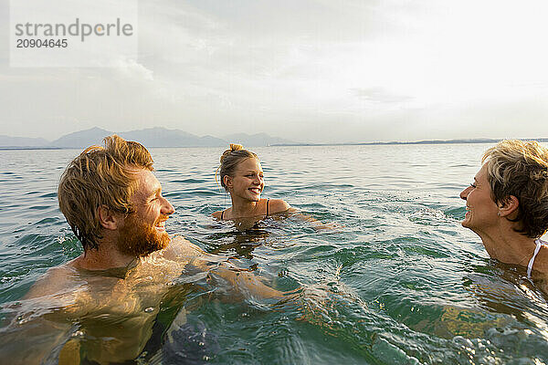 Three friends enjoy a refreshing swim in a tranquil sea at sunset  sharing laughter and a warm connection.