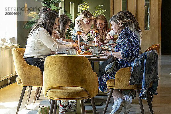 A group of women enjoy a meal together at a stylishly furnished restaurant with golden velvet chairs and warm lighting.