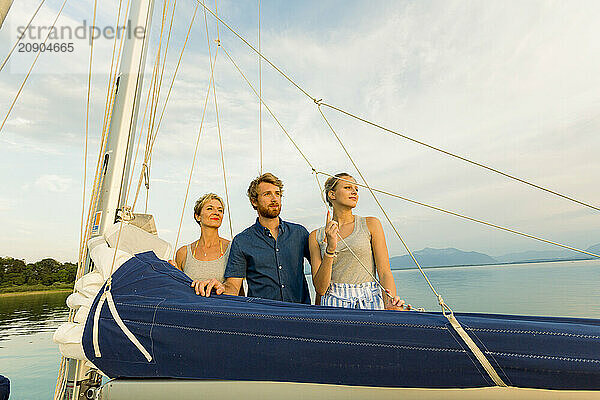 Three friends enjoying a sailboat ride at sunset with a clear sky in the background.