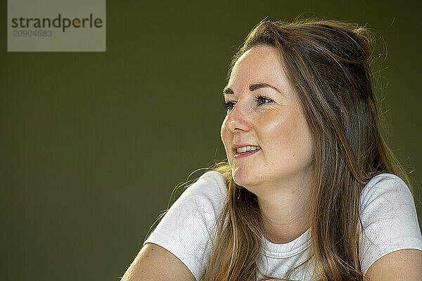 Smiling woman with long hair looking to the side against a green background.