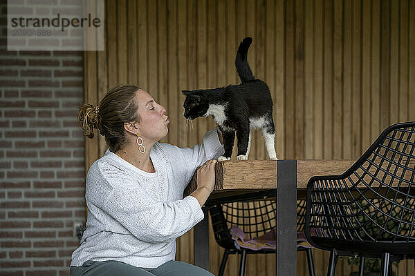 Woman interacts affectionately with a black and white cat perched on a wooden table.